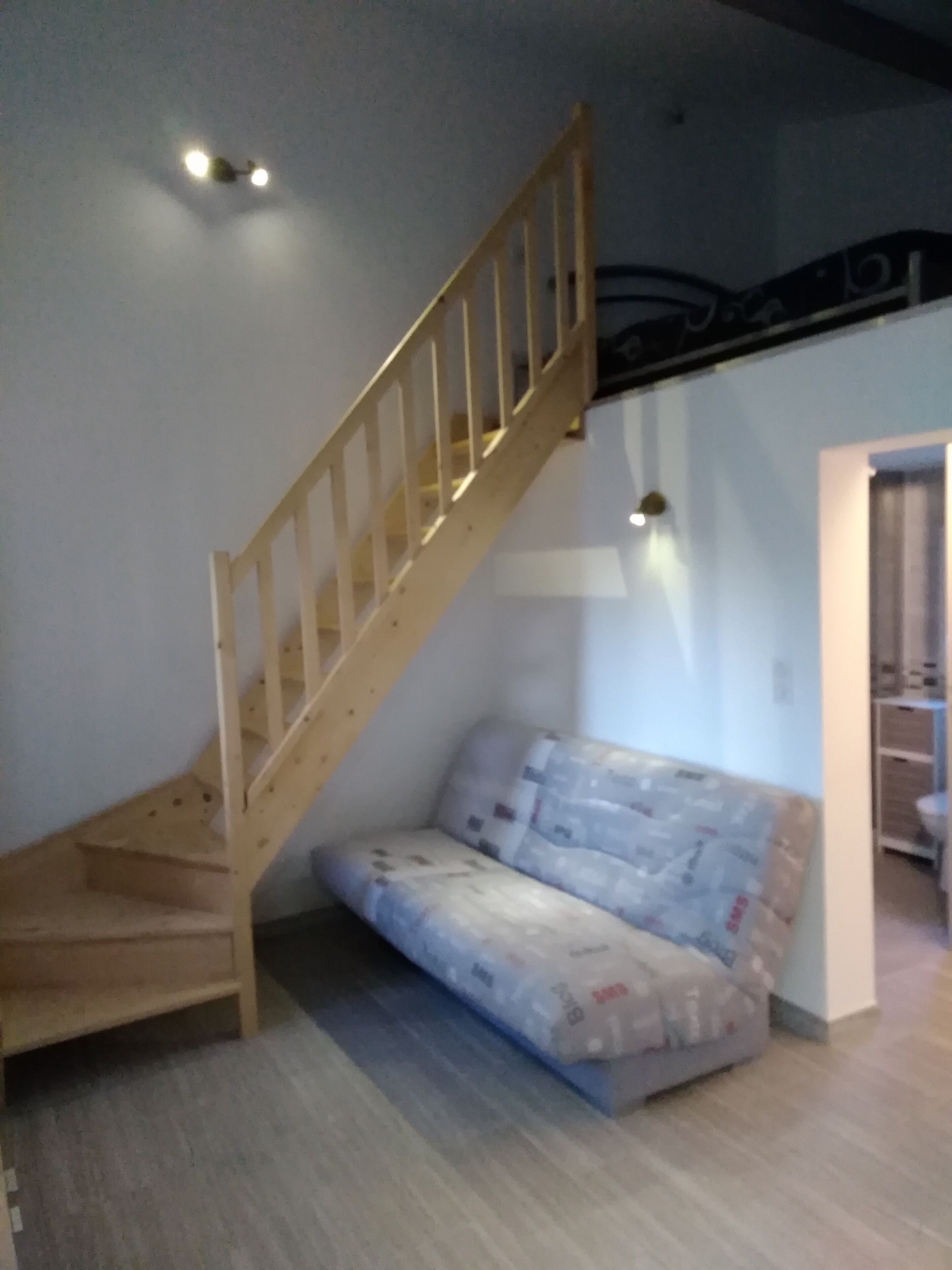 A room with a wooden staircase, a sofa covered with protective sheets, and a wall-mounted light fixture.