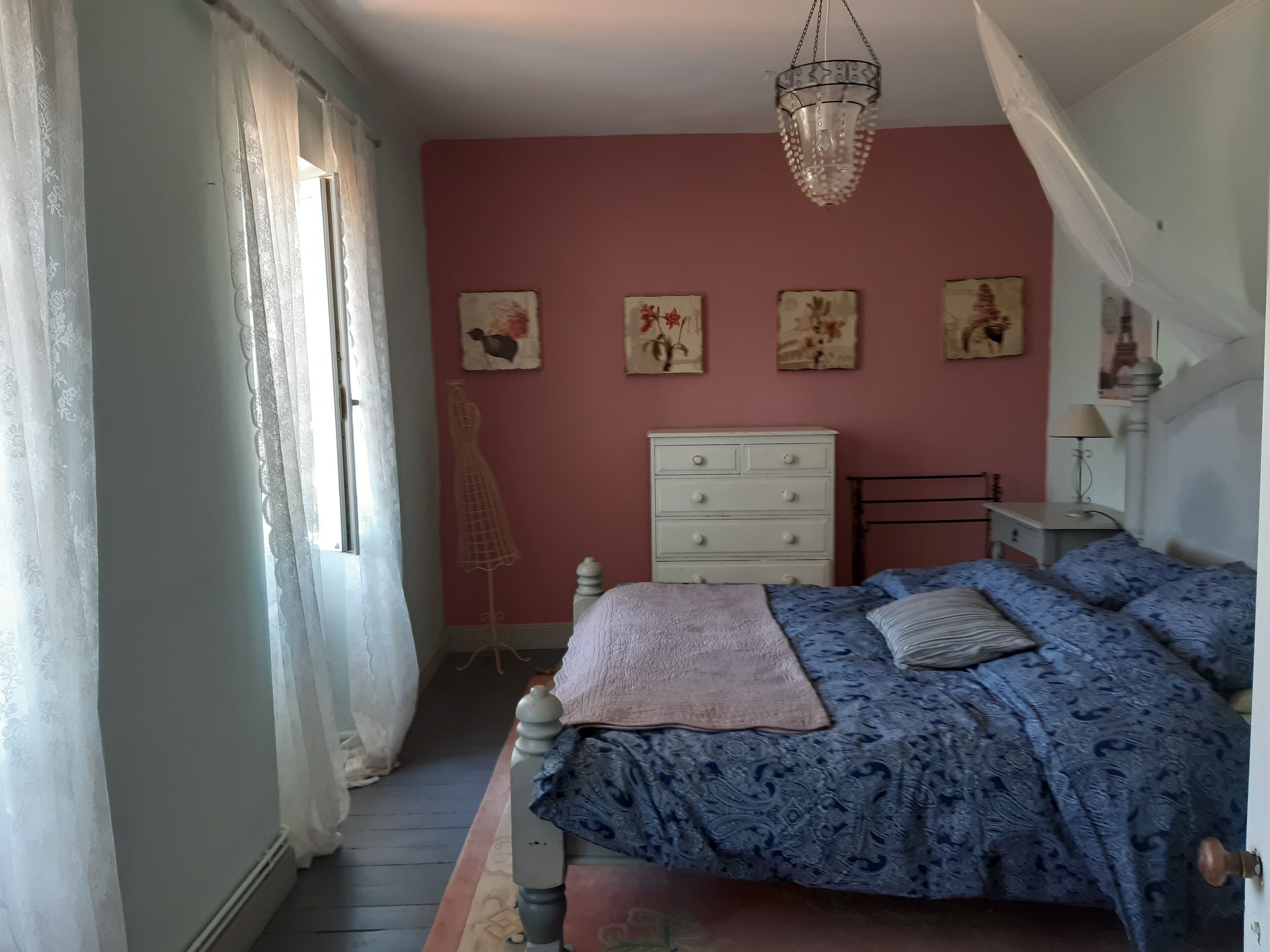 A bedroom with a bed, dresser, and a hanging light fixture.
