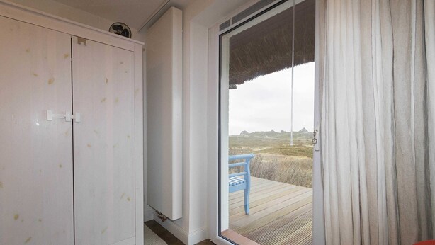 A room with a sliding glass door leading to an outdoor deck, a white wardrobe, and a blue chair on the deck.
