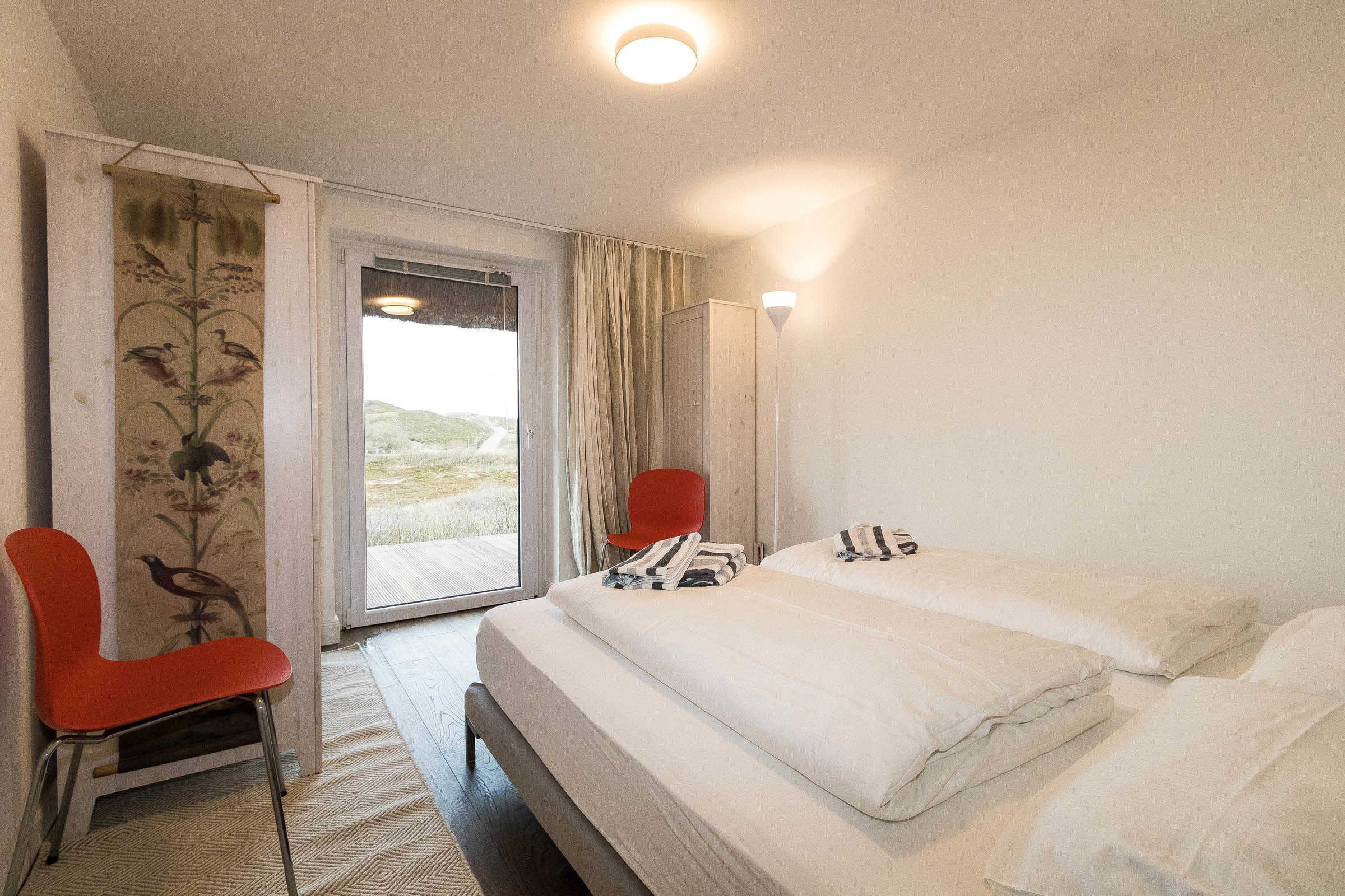 A hotel room with a bed, a red chair, a window with curtains, and a view of the outdoors.