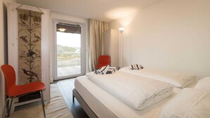 A hotel room with a bed, a red chair, a window with curtains, and a view of the outdoors.