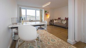 A modern living room with a white sofa, a dining table with chairs, and a large window.