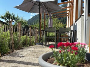 Een terras met een pergola, stoelen en een tafel, omringd door een tuin en uitzicht op een berg.