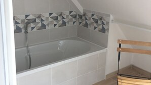 Un baño con bañera, ducha y una banca.