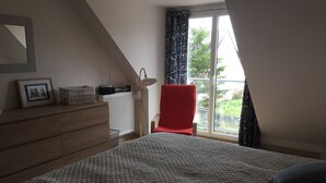 Un dormitorio con cama, cómoda, radiador, silla y ventana con cortinas.