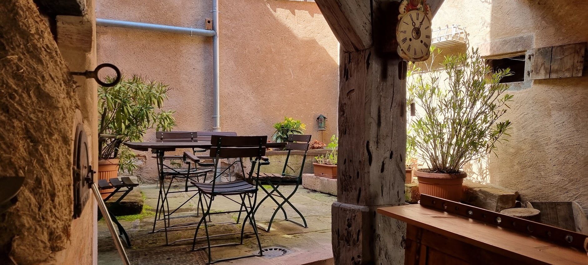 An outdoor patio with a table and chairs, surrounded by potted plants and a rustic wooden bench.
