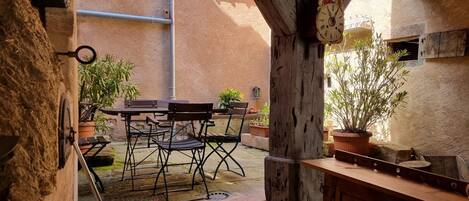 An outdoor patio with a table and chairs, surrounded by potted plants and a rustic wooden bench.