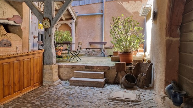 Une cuisine rustique avec un comptoir en bois, un sol en pierre et un four en pierre. Des marches mènent à un espace extérieur aménagé avec un banc et des plantes en pot.