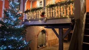 Un bâtiment traditionnel doté d’un balcon décoré pour Noël, avec des guirlandes lumineuses et des éléments de verdure.