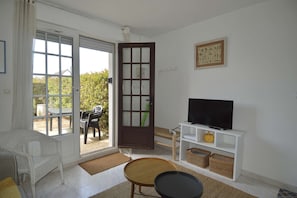 A room with a television, wicker chair, and a door leading outside. - Triplex with garden - wifi - 400m from the beach (Courseulles-sur-Mer)