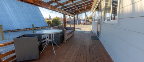 A covered outdoor area with a wooden deck, a round table, and a sofa.