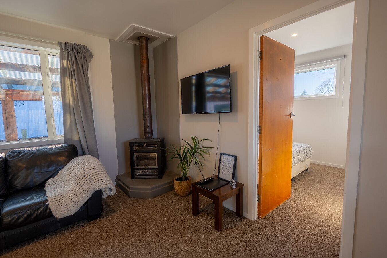 A cozy living room with a fireplace, a TV mounted on the wall, a comfortable sofa, and a door leading to another room.