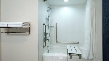 Ein modernes Badezimmer mit barrierefreier Dusche, Haltegriffen, einem weißen Handtuchhalter und einem kleinen Waschbecken.