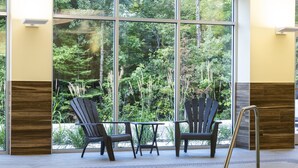 Una piscina interior con dos sillas Adirondack y una mesita, ventanas amplias con vistas a árboles y suelo de baldosas.
