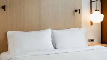 Una cama bien tendida con sábanas blancas, cabecera de madera y lámpara de pared.