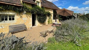 Une maison en pierre avec un toit en tuiles, un patio couvert avec des meubles d’extérieur et un jardin agrémenté de plantes de lavande.