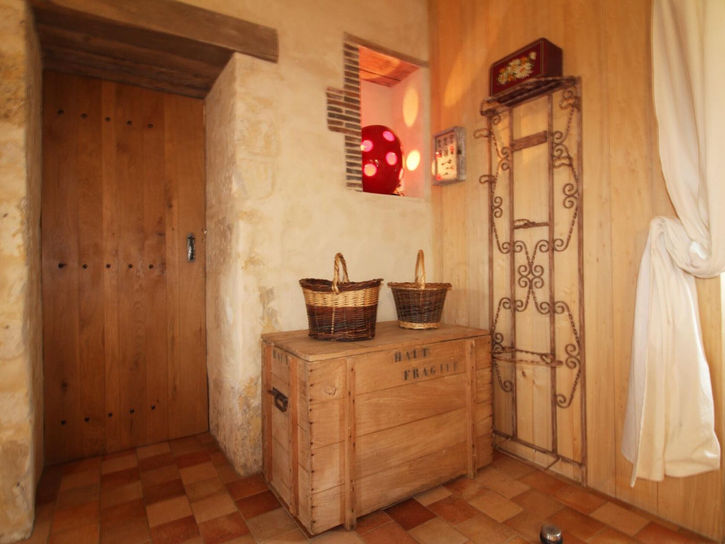 Een rustieke kamer met een houten deur, een klein raam met een rood licht, een houten kist met de tekst 'FRAGILE', en een metalen hek.