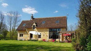 Una casa de dos pisos con un jardín grande, un patio con mobiliario exterior y una chimenea.