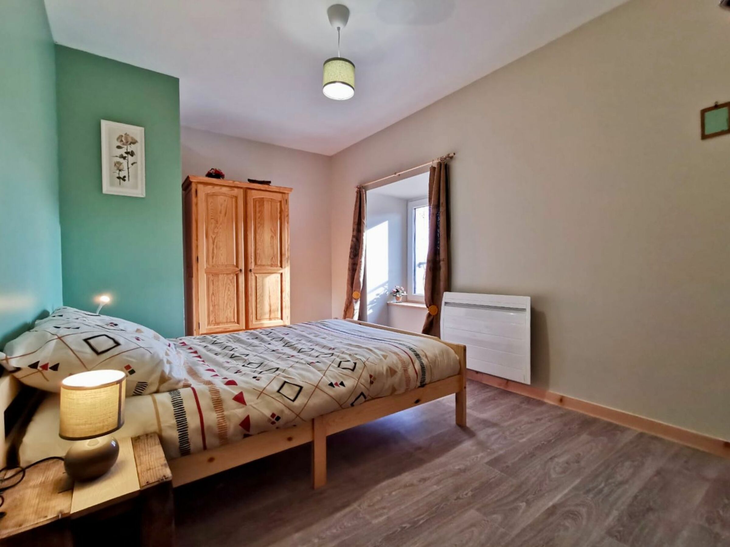 A bedroom with a bed, a wooden wardrobe, a bedside lamp, and a radiator.