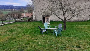 A rustic stone building with a red-tiled roof, a small wooden structure, and a grassy yard with outdoor seating. - Renovated cottage in the heart of Auvergne (Arlempdes)