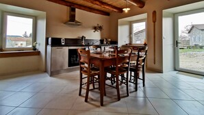A spacious kitchen with a wooden table and chairs, a built-in oven, and a window overlooking a garden. - Renovated cottage in the heart of Auvergne (Arlempdes)