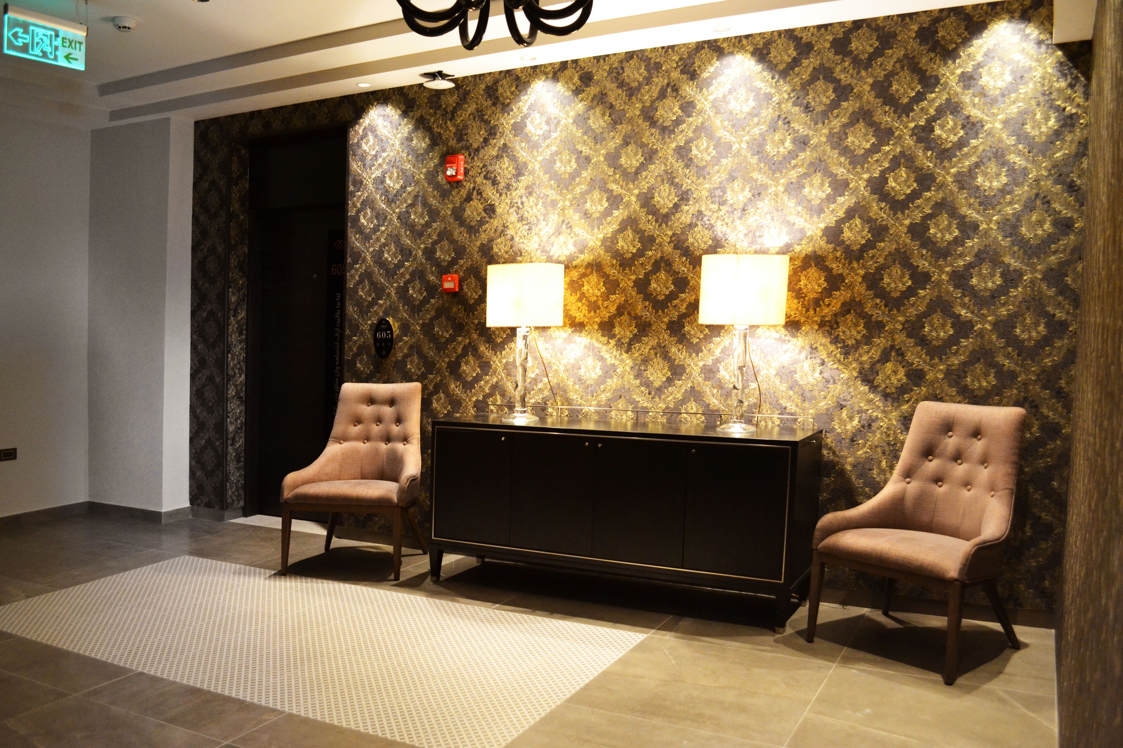 A lobby with two armchairs, a console table, and patterned wallpaper.