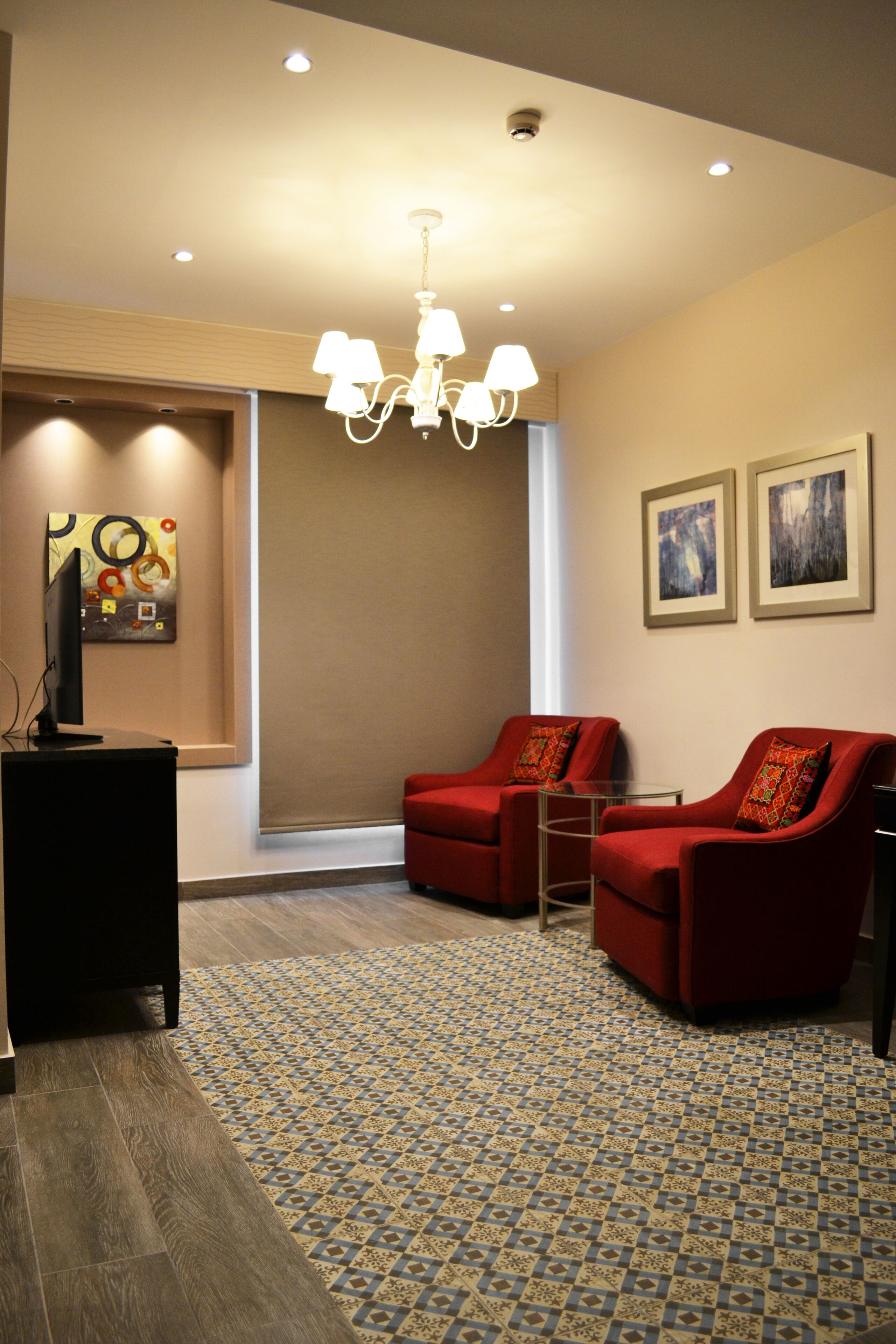 A modern living room with a television, red armchairs, a patterned rug, and a chandelier.
