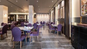 A spacious restaurant with high ceilings, modern lighting, and a patterned wall in the background. - Ambassador Hotel Amman, a Boutique Hotel (Amman)