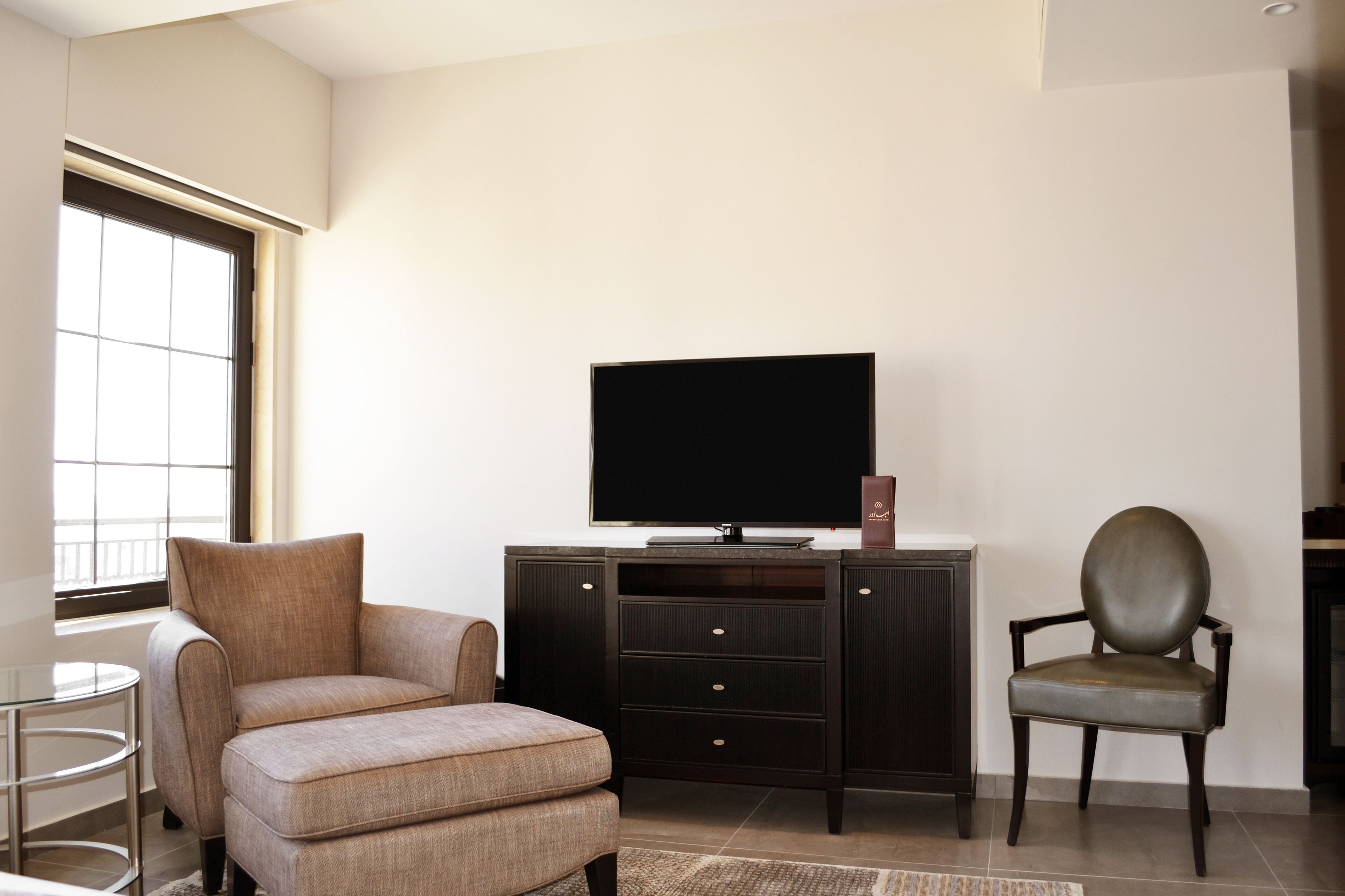 A modern living room with a sofa, a television on a dark wooden cabinet, a chair, and a small round table.