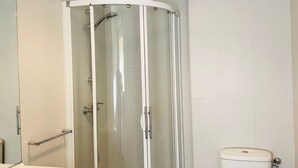 A bathroom with a glass-enclosed shower, a toilet, and a sink with a mirror.