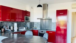 A modern kitchen with red cabinets, a stainless steel range hood, a microwave, and a round dining table with chairs.