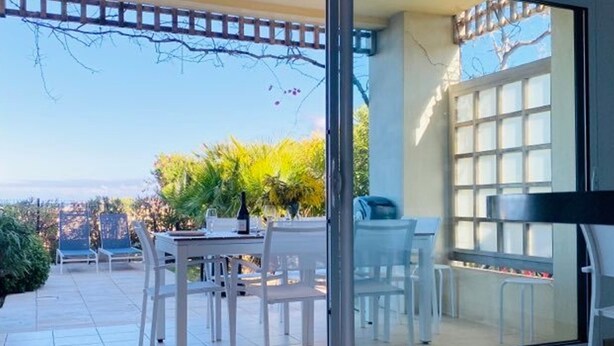 A modern patio with a glass door leading to a dining area, featuring a table and chairs, and a view of the cityscape.