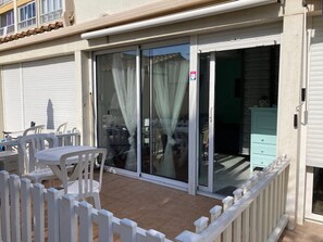 A patio with a table and chairs, a sliding glass door, and a white picket fence. - Charming Ground-Floor Studio with Pool, Terrace, Secured Parking, and Amenities for 2 (Cap d'Agde naturisme)