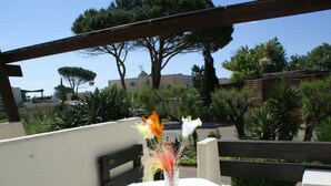 An outdoor dining area with a table set for two, surrounded by greenery and a wooden pergola.