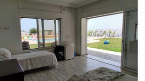 A hotel room with two beds, a large window, and a view of a pool and greenery outside. - Very large villa ideal for groups of up to 15 to 18 people (Kélibia)