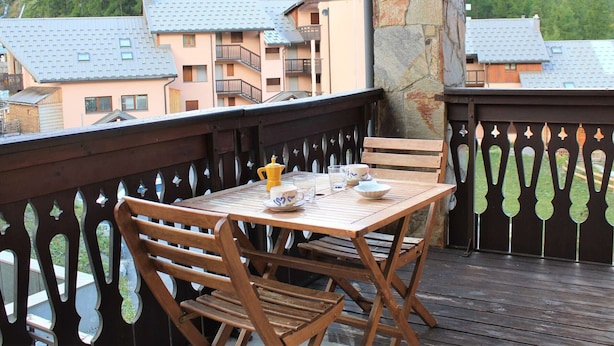 A wooden deck with a table and chairs, overlooking a mountainous area with buildings. - Cozy 2-Bed Apartment with Balcony, 100m from Slopes and Shops in Vars Les Claux (Vars)
