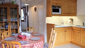 A cozy kitchen with wooden cabinets, a microwave, and a dining area set with a table and chairs. - Cozy 2-Bed Apartment with Balcony, 100m from Slopes and Shops in Vars Les Claux (Vars)