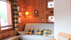 A cozy room with a wooden wall, a sofa with checkered cushions, a small wooden table, and a lamp. - Cozy 2-Bed Apartment with Balcony, 100m from Slopes and Shops in Vars Les Claux (Vars)