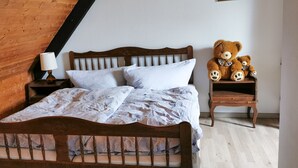 A wooden bed with white linens, a nightstand with a lamp, and two teddy bears on a small table beside the bed. - Cozy terraced vacation home with wood-burning fireplace (Bernau im Schwarzwald)