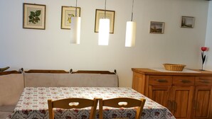 A dining area with a table set for two, a wooden cabinet, and framed artwork on the wall. - Cozy terraced vacation home with wood-burning fireplace (Bernau im Schwarzwald)