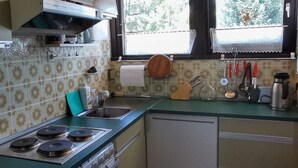 A kitchen with a gas stove, a sink, and a window with a view of trees. - Cozy terraced vacation home with wood-burning fireplace (Bernau im Schwarzwald)