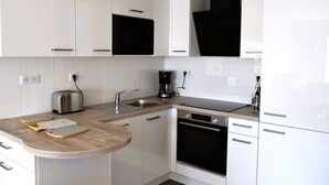 A modern kitchen with white cabinets, a stainless steel toaster, a sink, a coffee maker, and a built-in oven. - 1-bed apartment, garage, direct beach access (Les Sables-d'Olonne)