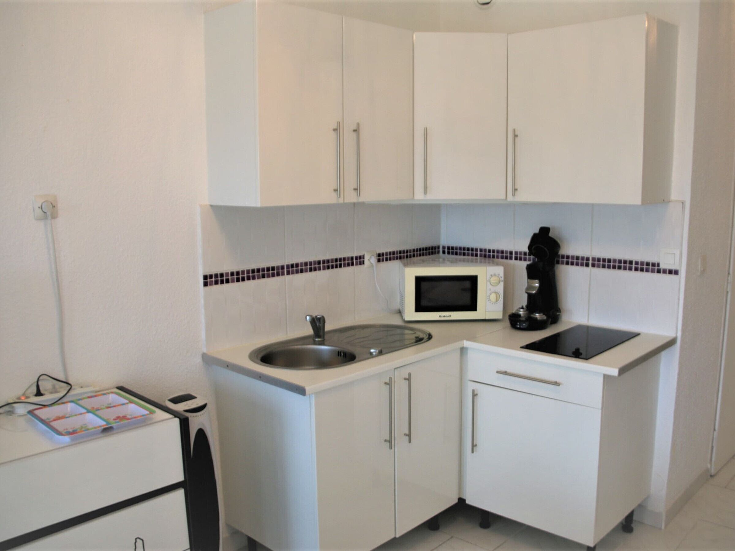 A small kitchenette with white cabinets, a microwave, a coffee maker, and a sink.