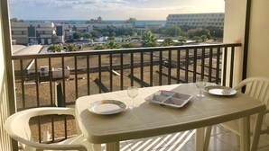 Un balcon avec une table et des chaises, donnant sur un parking et des immeubles.