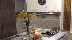 Uma mesa de jantar posta com pratos, copos e talheres, um vaso com flores amarelas e uma vela acesa.