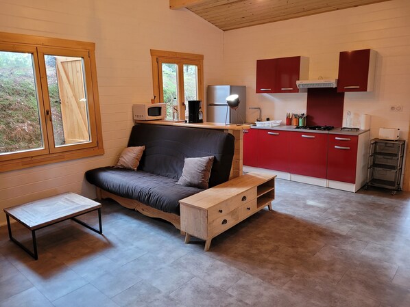 Espaço compacto com sofá, mesa pequena e área de cozinha compacta com armários vermelhos e micro-ondas.