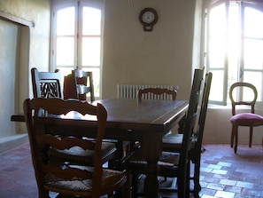 Enjoy meals in this dining area with a large table and six chairs, surrounded by large windows and a wall-mounted clock.