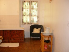 Cozy kitchen area with a wooden floor and white walls, featuring a cabinet, window, and comfortable seating.