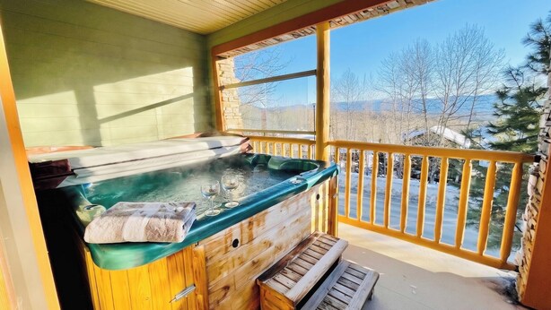 Un jacuzzi en una terraza de madera con vista a un paisaje nevado y árboles.