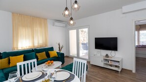 Un salon moderne avec un canapé vert, une table à manger pour deux personnes et un téléviseur à écran plat fixé au mur.